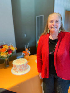 Photo of retiree Cathy Dunn standing next to orange and white decorated cake at EPC event