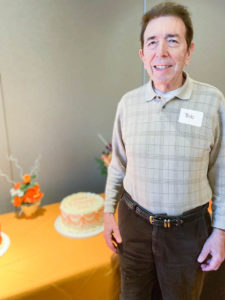 Photo of Bob Williams standing next to orange and white decorated retirement cake at EPC event.
