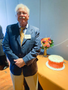 Photo of Steve McCallum standing next to orange and white decorated retirement cake at EPC event.