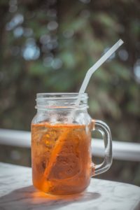 Photo of a mason jar filled with sweet tea and a straw, set on an outdoor table.