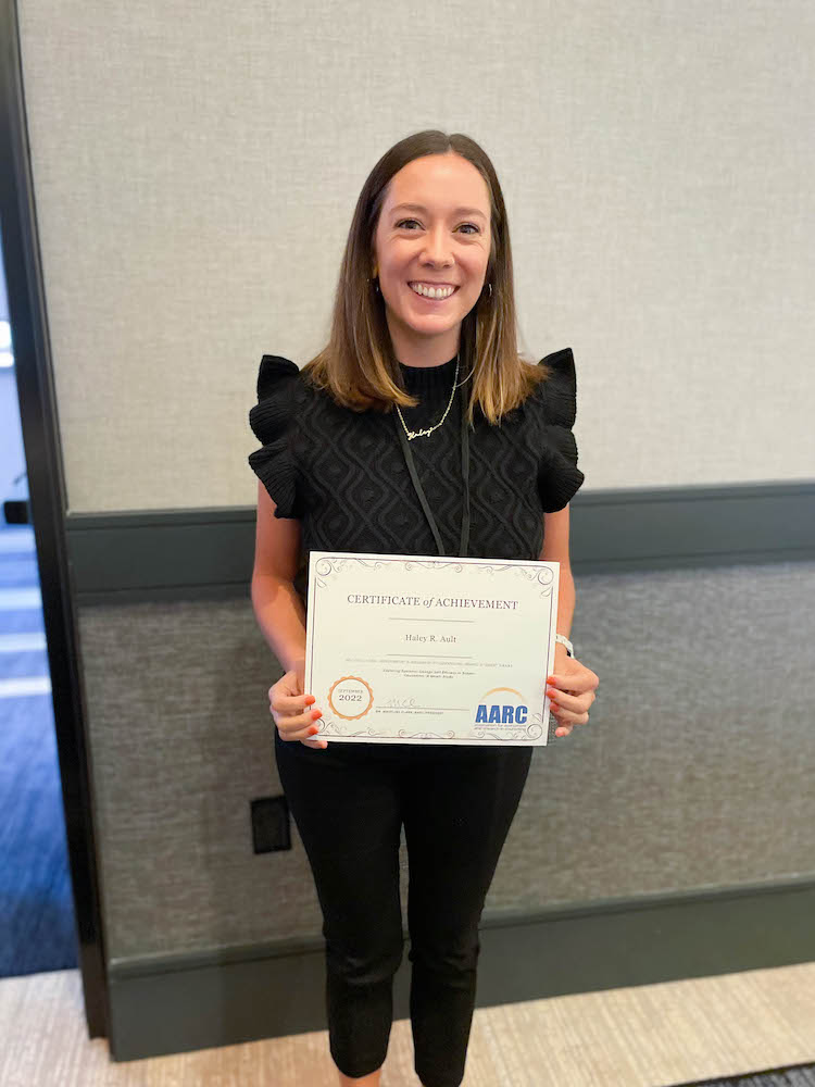 Photo of Haley Ault holding certificate for a grant awarded from AARC at the 2022 conference